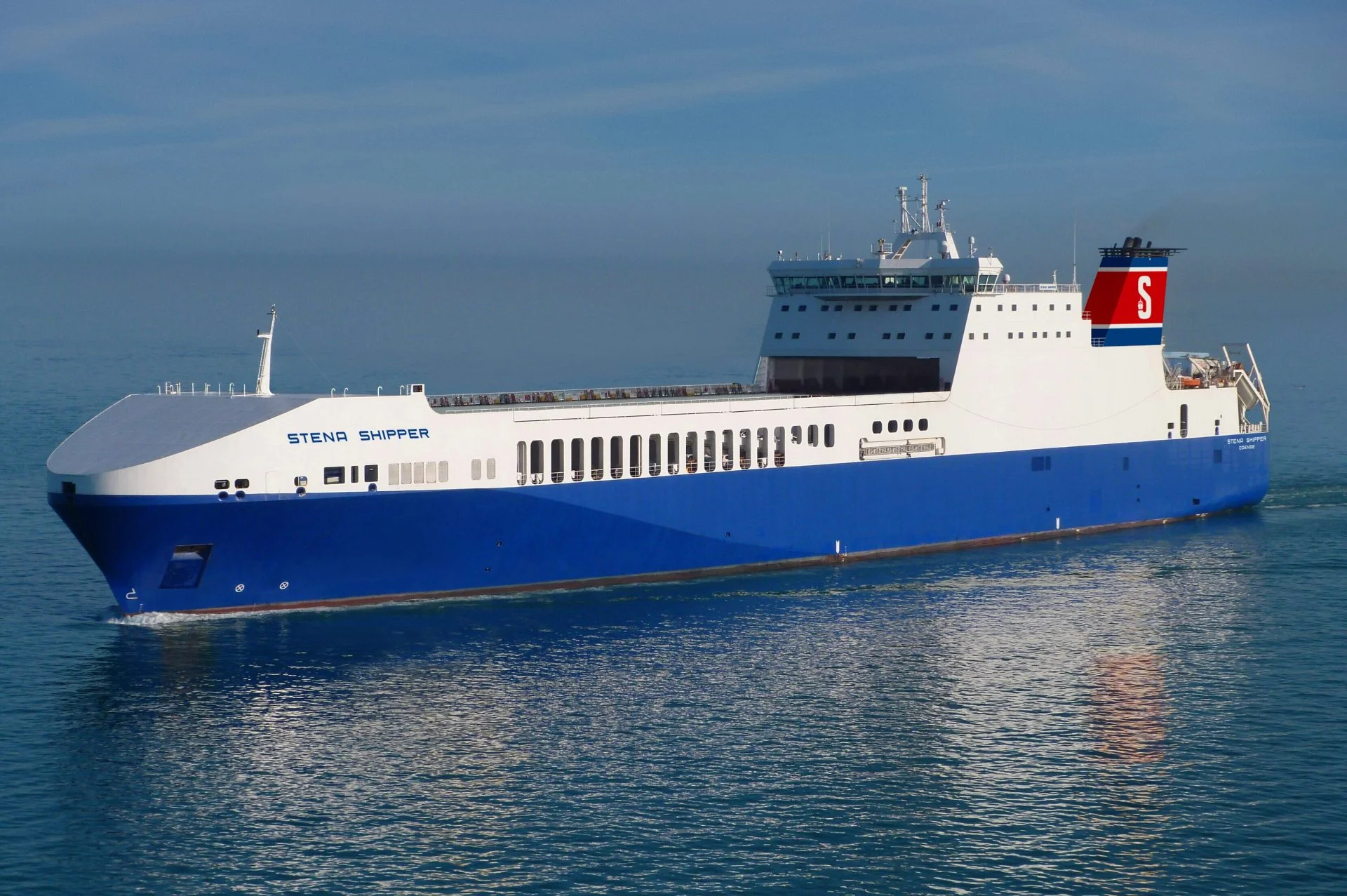 Large blue and white cargo ship with "Stena Shipper" on the side, sailing on calm waters under a clear blue sky.